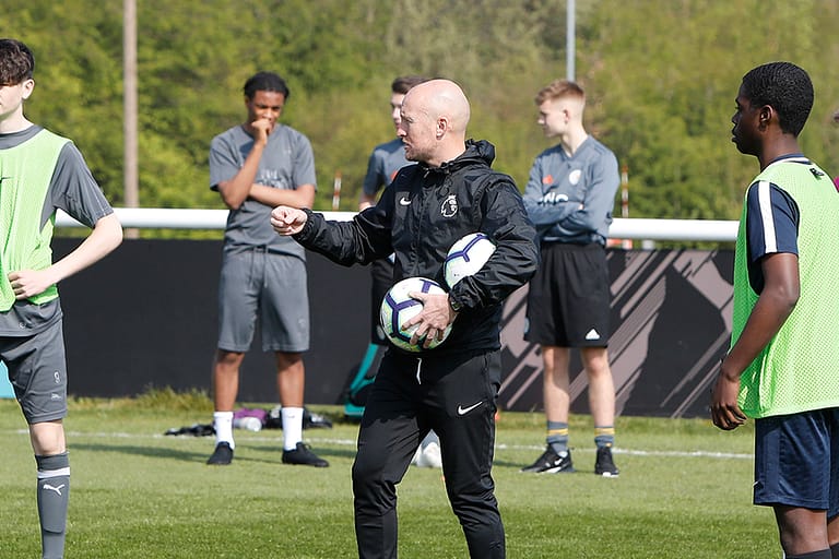 soccer coach holding soccer ball and talking to players